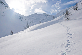 Footsteps in the snow with mountains and sunshine in the background