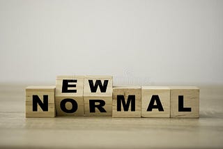 Wooden blocks with the phrase new normal slightly tilted upward in black lettering.