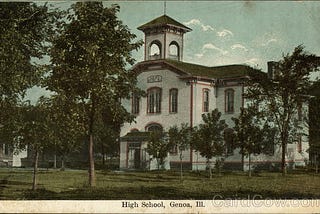 An old post card showing a two-story, white school building. The building is surrounded by trees and green grass, and the sky is blue. The post card says “High School, Genoa, Ill.”