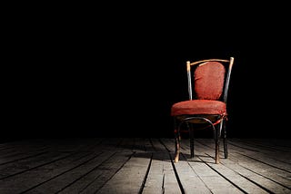 a single wooden chair on a wooden planed floor in a dark room