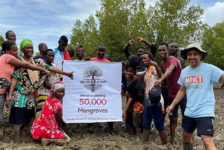 A group of people standing happily around a banner that reads “join us in planting 50,000 mangroves.”