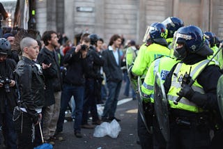 Group of protesters stand facing group of armoured police