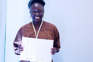 A young african adult wearing brown and holding a Macbook Air.