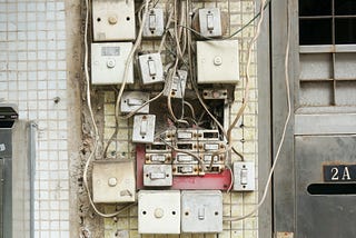 Lots of light switches, close together, and surrounded by multiple cables