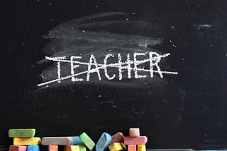 colored chalk sitting by a blackboard with the word “teacher” crossed out