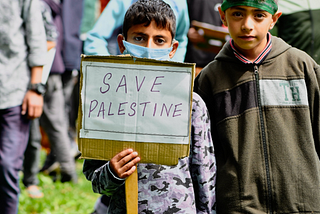 A boy holds a handwritten sign that says “Save Palestine.”