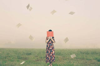 A dream scene shows a woman standing in the middle of a grass field, hiding her face behind a book while the pages fly away.