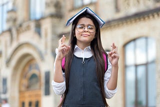 School girl stands with book open on her head crossing her fingers for luck.