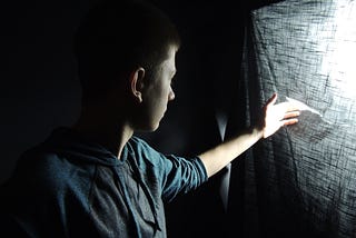 Boy touching a tear in a grey curtain