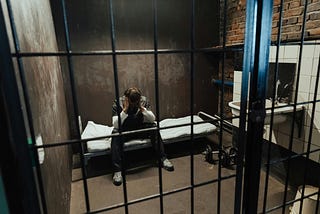 A young man sits in a prison cell, head in hands.