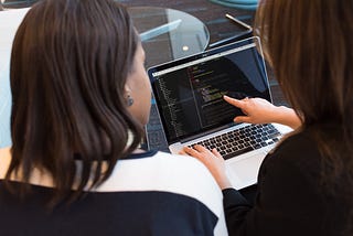 Two people looking at code open on a Mac computer