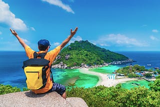 Traveller sitting on top of a rock overlooking a beautiful beach and mountain