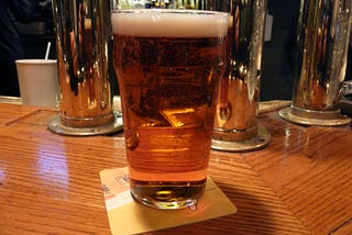 a full pint glass of beer sitting on a wooden bar