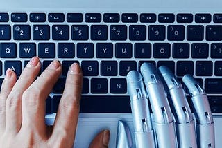 A human hand and a cyborg hand typing on a keyboard.