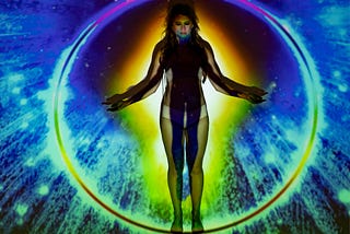 A woman in underwear bathed in colorful projected lights that resemble a human aura