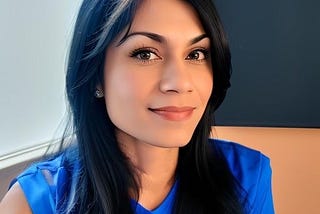 Indian woman with black hair wearing a blue t-shirt. She has a huge smile on her face.