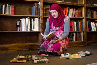 Girl wearing hijab and reading a copy of Harry Potter and the Sorcerer’s Stone.