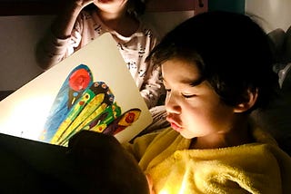 Boy reading The Very Hungry Caterpillar to a girl by flashlight.