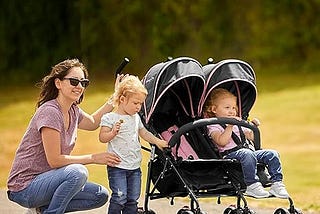 A mother with her 2 baby girls on a double pink and black color baby stroller