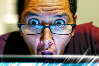 Vivid photo portrait of a very surprised Hispanic man with glasses, behind a computer, text from the computer screen is reflected on the glasses