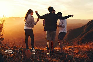 four friends dancing on a mountain at sunset