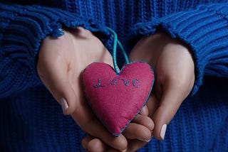 Person in blue sweater holds a pillow heart as a gift that reads “love.” https://www.amazon.com/Some-Assembly-Required-Organ-Transplant/dp/1684337364