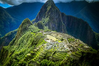Photo of very green mountain-ridge citadel Machu Picchu in Peru against dark mountains under a cloudy sky.