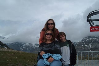 The author with her two children on a mountain in Zermatt. Her daughter is sitting in a wheelchair and her son is leaning against his mom and sister.
