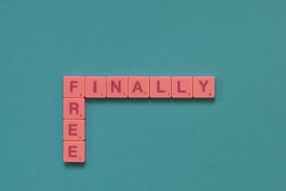 A solid background with plastic squares that have a single letter on each of the squares arranged to spell “Finally Free”.