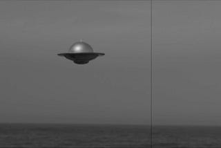 A classic black and white photo of a flying saucer over the ocean, like one from an old Hollywood UFO movie.