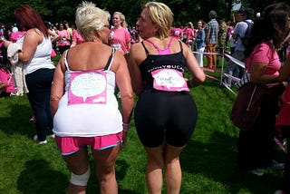 Two women sticking out their butts at a Race for Life UK event with other participants in the background.