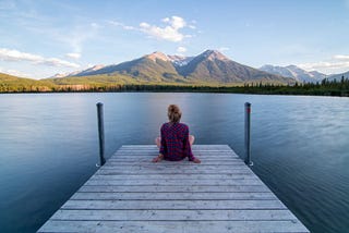 Woman at the edge of dock staring out at mountains in the distance, intended to invoke the sense of pondering life and its wonders
