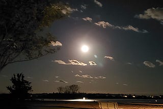 The full moon over Long Island Sound with a bench in the middle ground and grass in the foreground