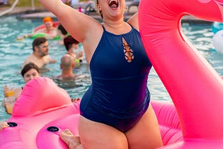 lady in swimsuit on inflatable pink flamingo with her arms in the air