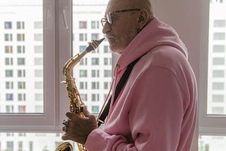 a bald man in a pink hoodie plays the saxophone
