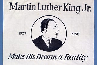 White fabric banner with black text “Martin Luther King Jr. / Make His Dream a Reality” and image of man in suit