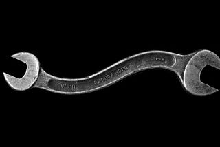 A double ended silver wrench that is curved in the middle, against a black backdrop