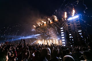 A crowd of people at a concert with flashing lights and fire.