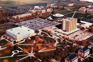 Aerial view of Bowling Green State University which includes Carillon Park (which I don’t believe was called that when I went to school there) in the foreground, with its array of sidewalks, Anderson Arena (now Memorial Hall) , Jerome Library, Saddlemire Student Services Building (a disc-shaped building), Moore Musical Arts Center, the Student Recreation Center, and part of the Kreischer Quadrangle (student housing).