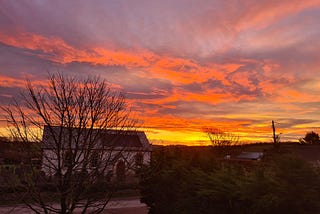 a methodist chapel behind a bare winter tree and above that is a vivid sunrise full of purple, orange and a streak of yellow