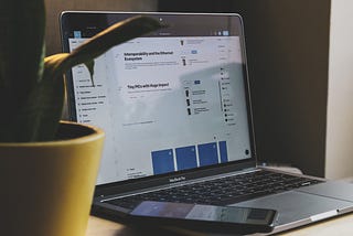 A laptop with the Figma app open and a phone laying on top of the keyboard sits next to a yellow potted plant.