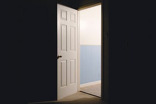An open door shows the way out of a dark room into a light corridoor.