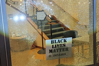 A shattered window with “First Christian Church, Disciples of Christ” at the top and a “Black Lives Matter” sign on a stick at the bottom.