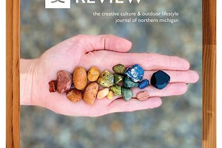 A photo showing the cover of The Boardman Review, which has a hand holding a spectrum of colorful beach stones.