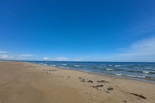 A sandy beach with small white waves on a blue sea.