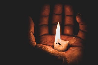 Hand holding lit candle stub in their palm.