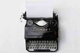 An old-fashioned black typewriter with a single sheet of white paper