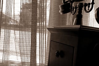 An antique telephone set with a backdrop of see through curtains