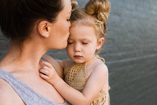 Young woman holding a young girl in her arms and kissing her forehead.