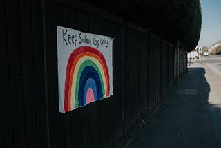 Poster stuck on a wall with a rainbow painted onto it. The words above the rainbow say ‘keep smiling, keep going’.